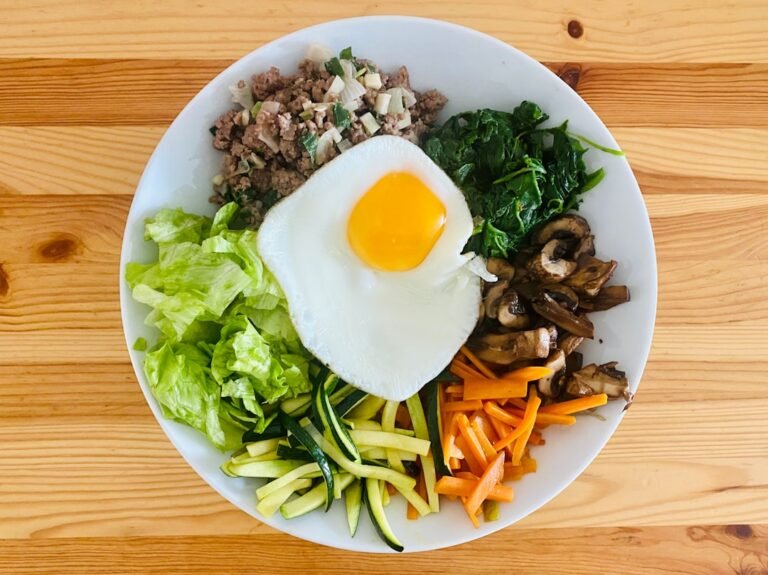 Bibimbap casero con huevo frito, carne, espinaca, zanahoria, zapallo y hongos